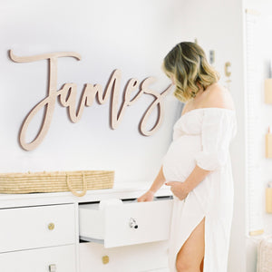 Wood Name Sign of "James" hung over dresser in baby boy nursery with pregnant mom standing by.
